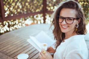 Portrait of smiling woman in shirt sitting at table reading. Happy she learned the 6 Benefits of Regularly Cleaning Your Septic System - Red Dirt Septic